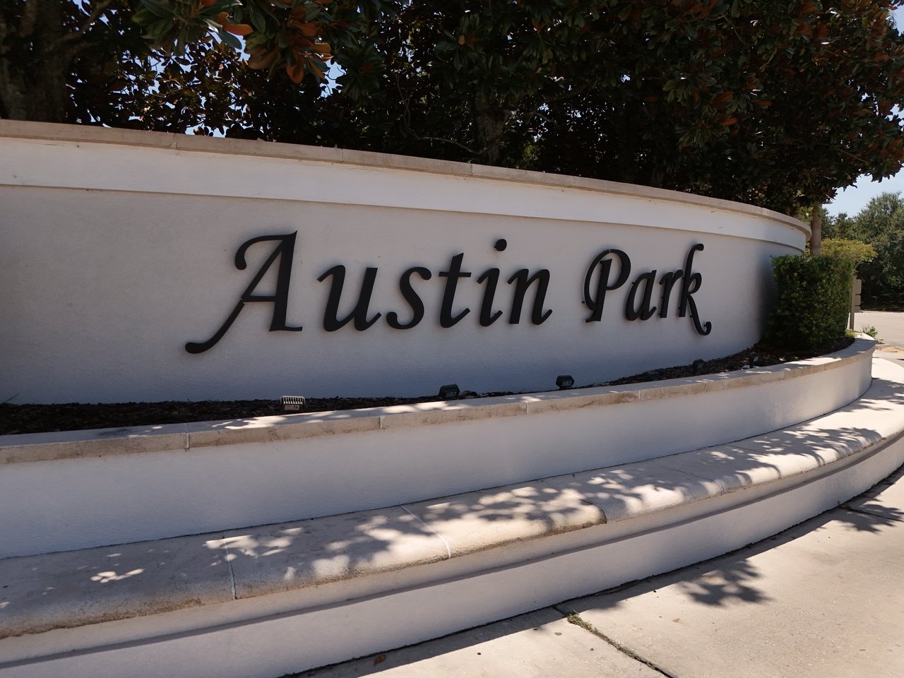 Austin Park entrance sign on a curved white wall beneath a leafy tree.