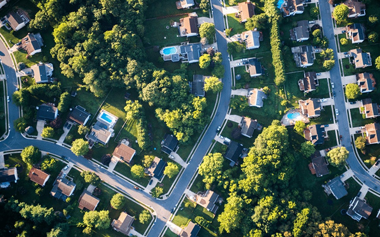 Aerial view of a tree-lined neighborhood with detached homes and backyard pools.
