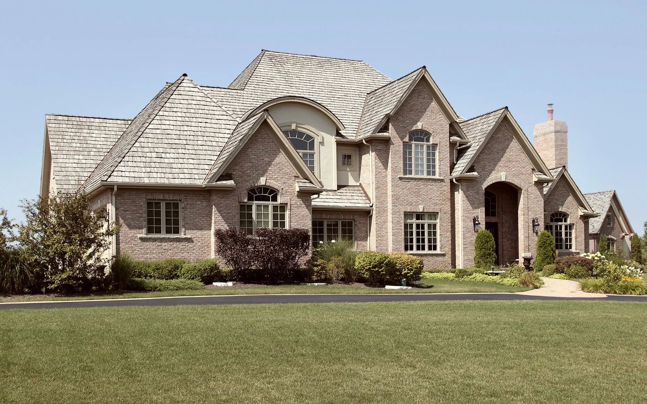 Large brick house with steep gables, an arched entry, and a broad green lawn.