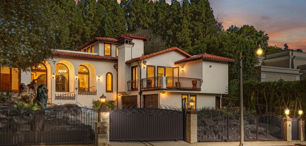 Spanish-style home with arched windows, a balcony, and an ornate gated entrance at dusk.