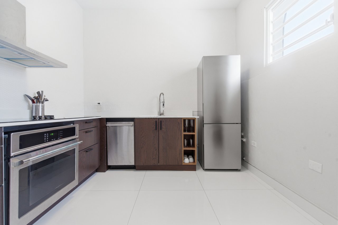 Modern kitchen with dark wood cabinets, stainless steel appliances, and a high window.