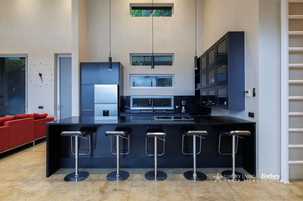 Modern kitchen with a black island, five bar stools, dark cabinetry, and pendant lights.