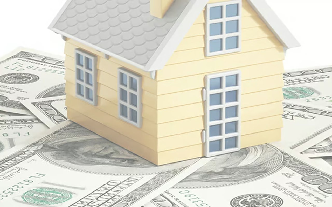 Yellow model house resting on U.S. dollar bills.
