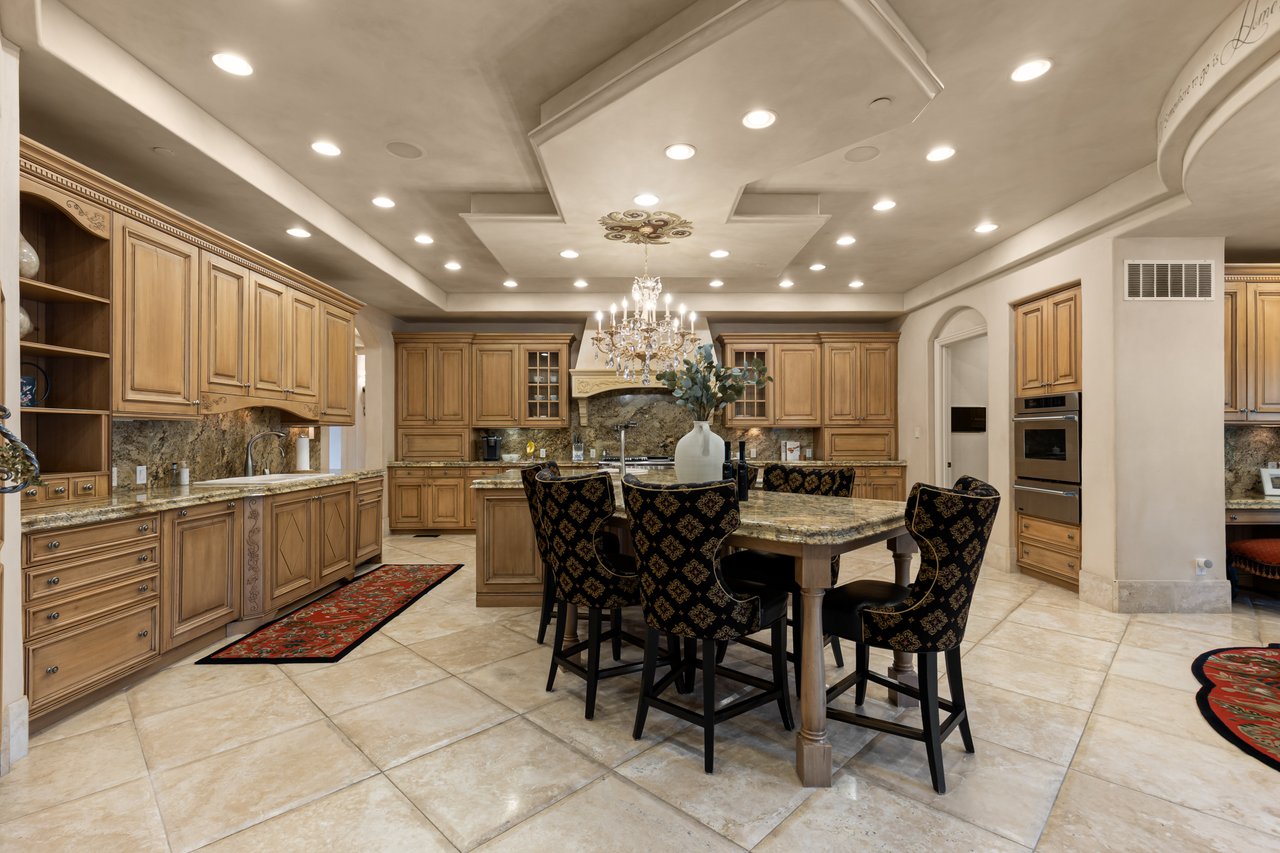 Spacious kitchen with honey-toned cabinetry, stone counters, and a dining table beneath a chandelier.