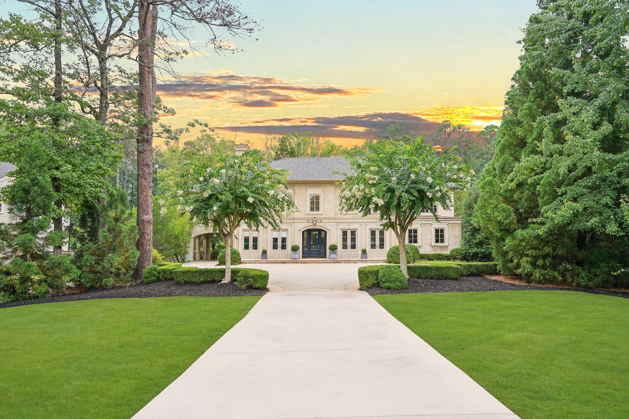 Cream-colored home with dark double doors, framed by flowering trees beneath a sunset sky.