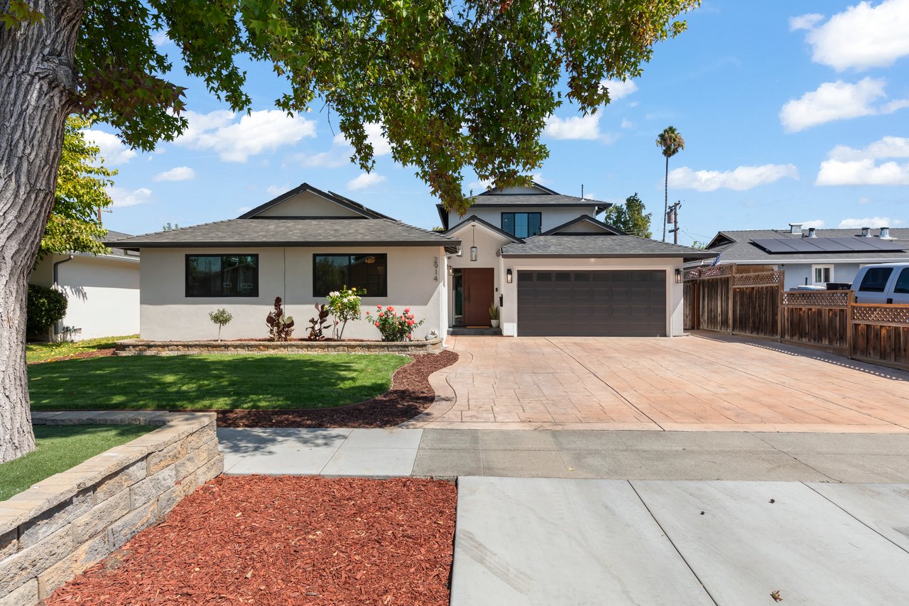 Home exterior with a broad paved driveway, two-car garage, and mature shade tree.