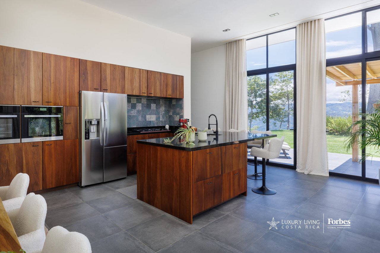 Modern kitchen with wood cabinetry and a large island beside windows overlooking a mountain valley.