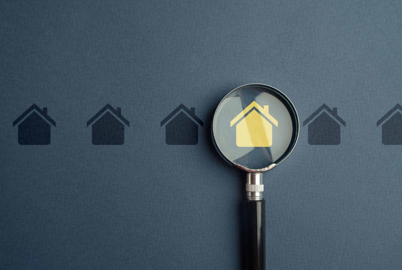 Magnifying glass highlighting a yellow house symbol among dark house icons.