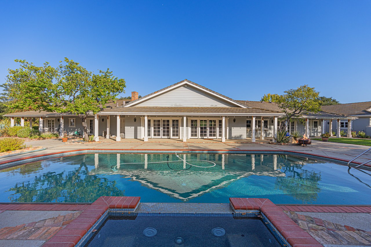Single-story home with a covered patio behind a large swimming pool and attached spa.