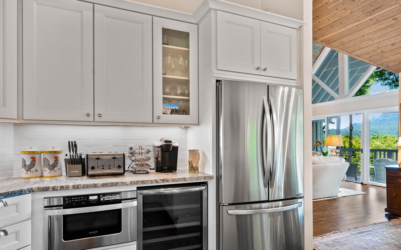 Kitchen with white cabinetry and stainless appliances opening to a vaulted living area with mountain views.