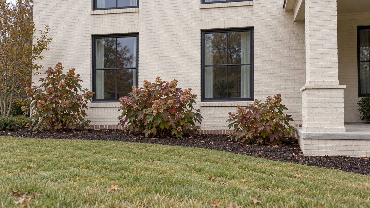 Ivory painted-brick home with charcoal-framed windows above oakleaf hydrangeas and a gently sloping lawn.