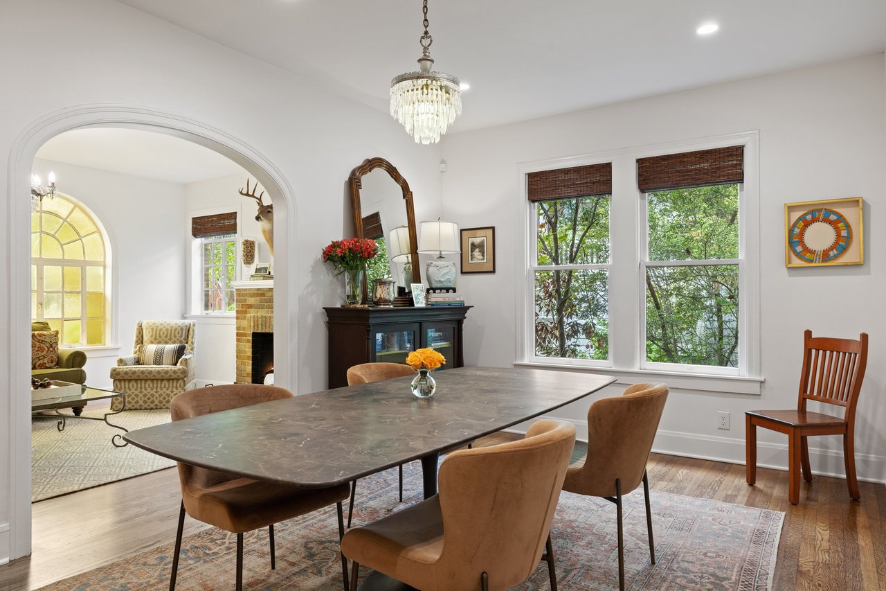 Dining room with a stone-top table, crystal chandelier, and arched opening to a sitting area.