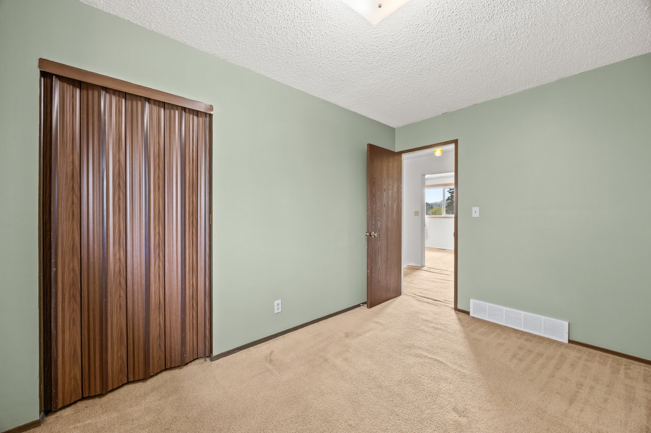 Unfurnished bedroom with beige carpet, pale green walls, and dark wood folding closet doors.