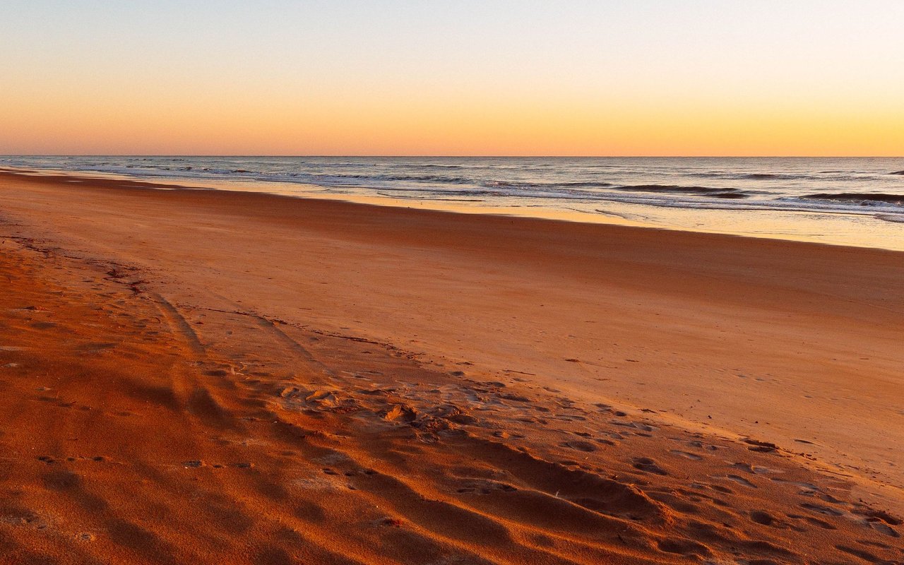 Ormond Beach shoreline at sunset, with orange sand and gentle waves.
