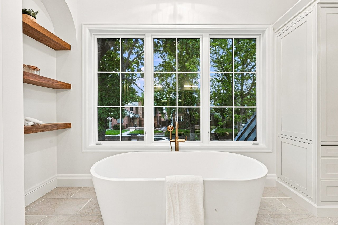 Bathroom with a freestanding soaking tub beneath a large window and open wood shelves.