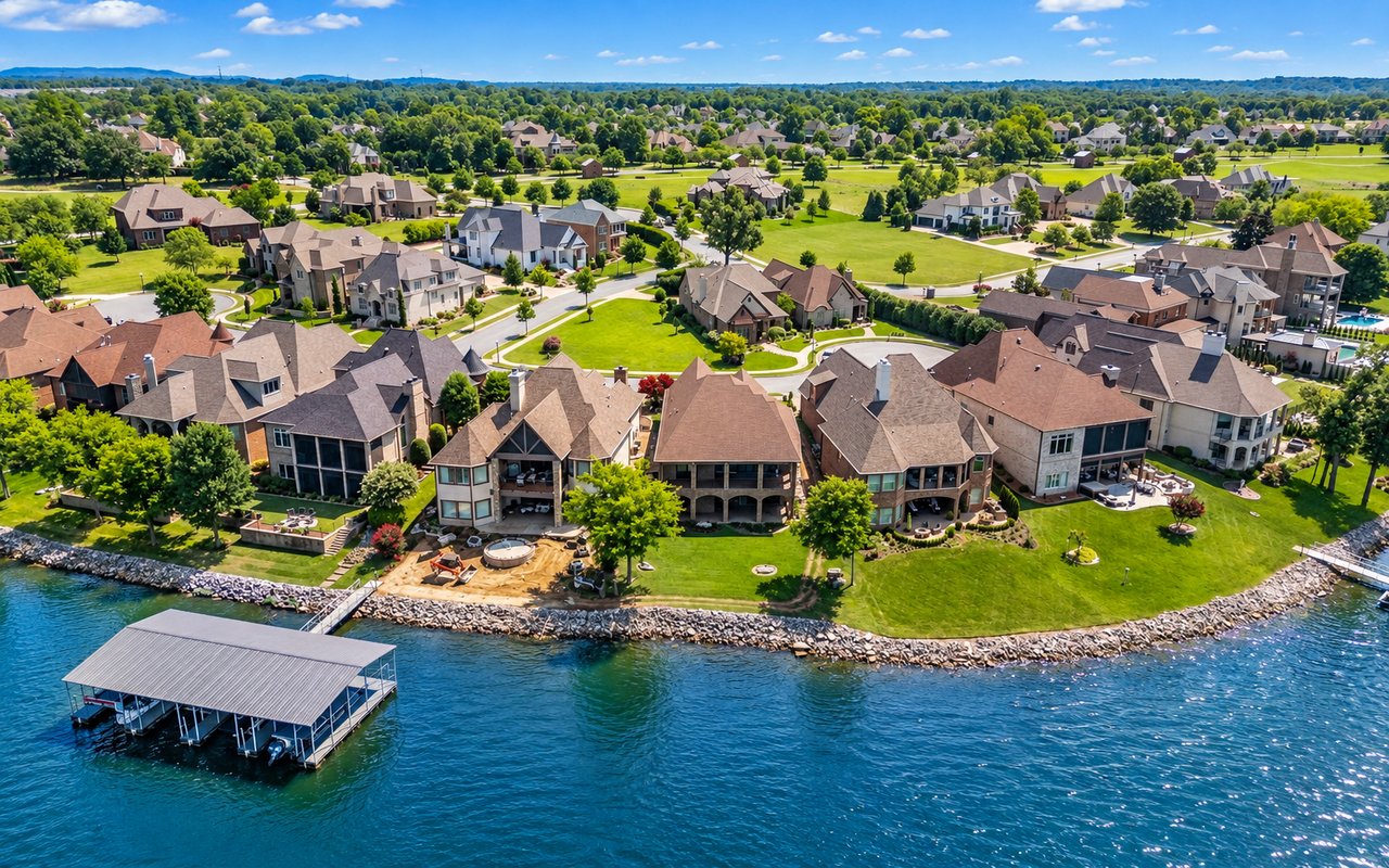 Aerial view of lakeside homes along a green shoreline, with a covered boat dock over the water.