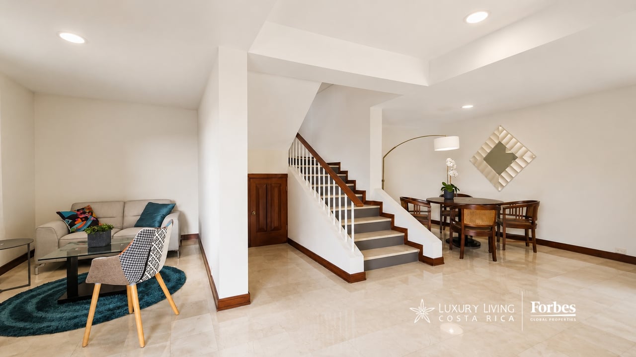 Furnished condominium living and dining area with a central staircase and polished tile floors.