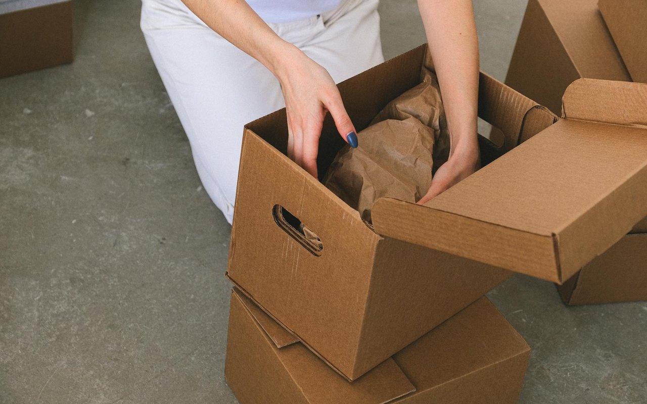 A person packs brown paper into a cardboard moving box stacked with other boxes.
