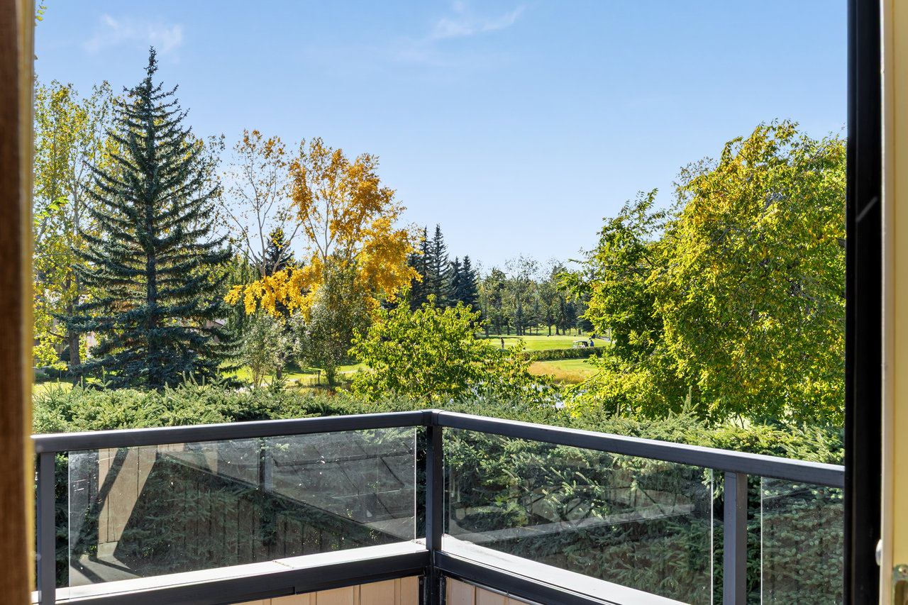 Glass-railed balcony overlooking a golf course framed by autumn trees.