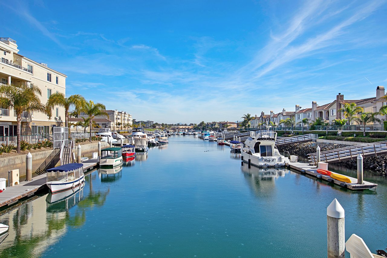 Channel Islands Harbor canal lined with moored boats, waterfront homes, and palm trees.