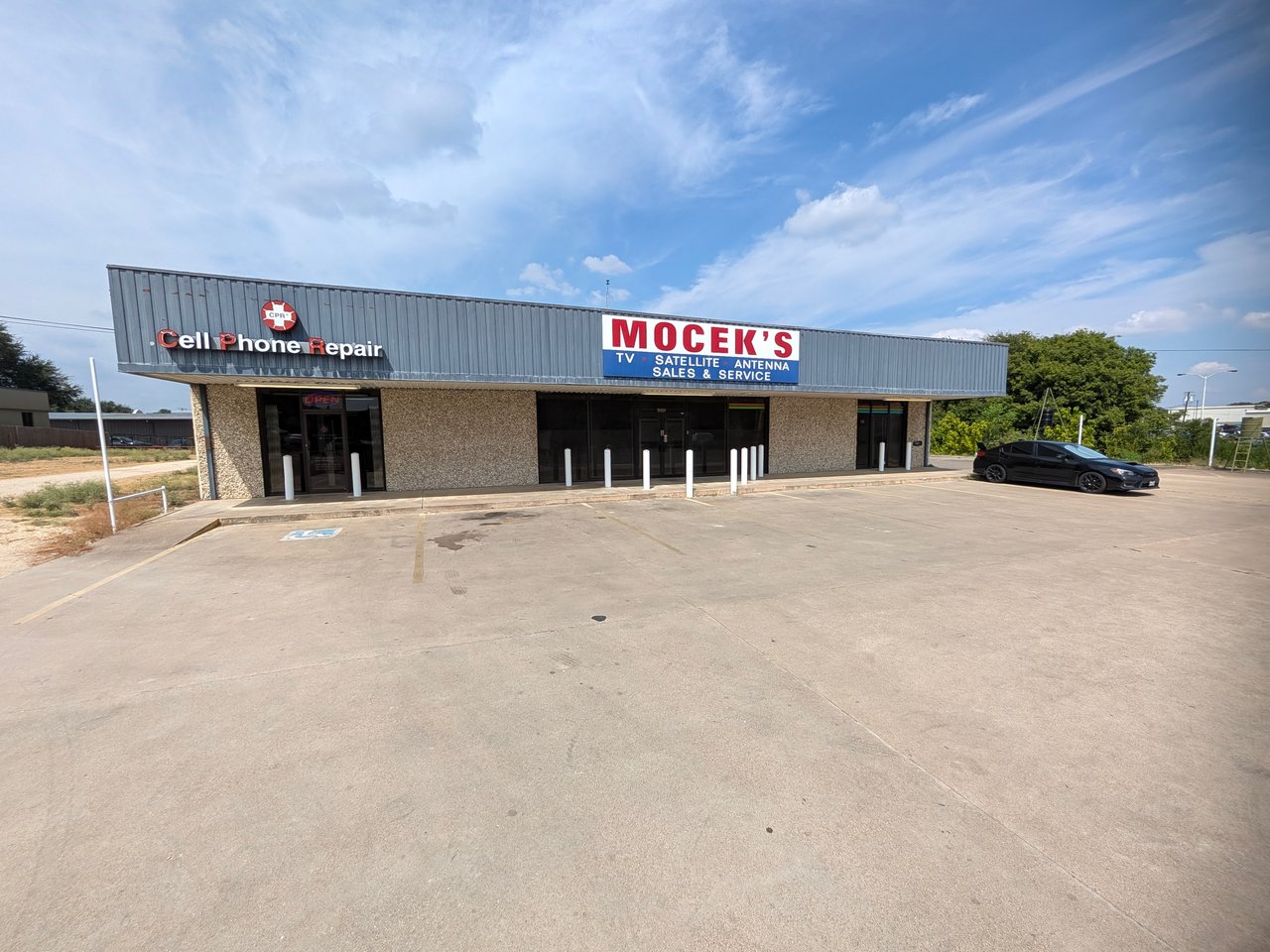 Commercial storefront with Cell Phone Repair and Mocek’s signs above a wide paved parking lot.