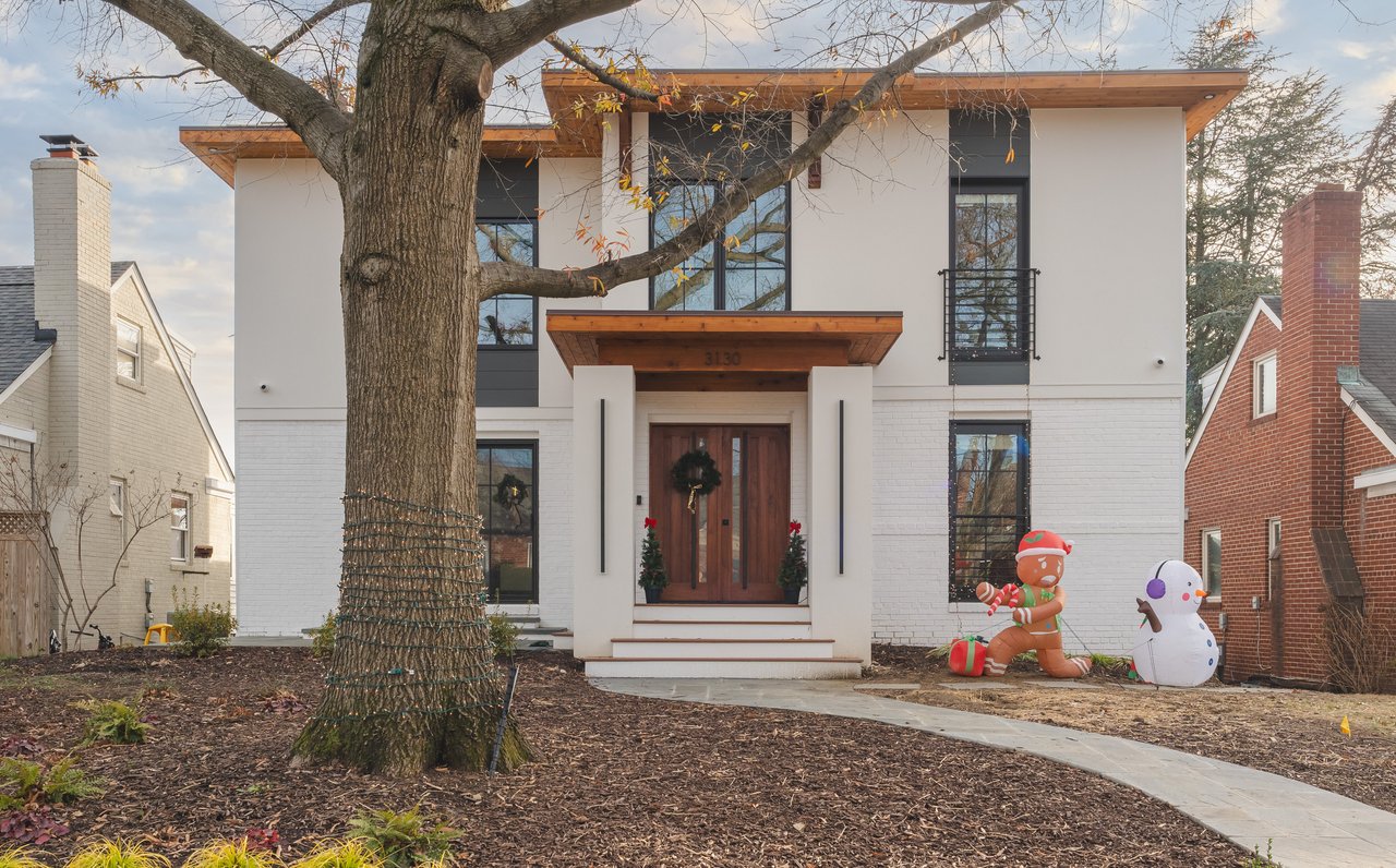 Modern white two-story home with a wood entry canopy, mature front-yard tree, and holiday inflatables.