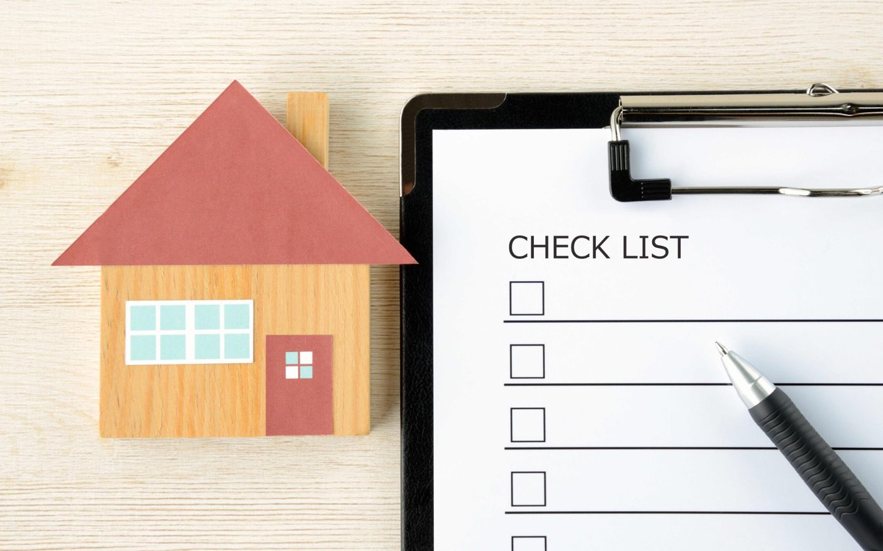 Wooden model house beside a blank checklist and pen