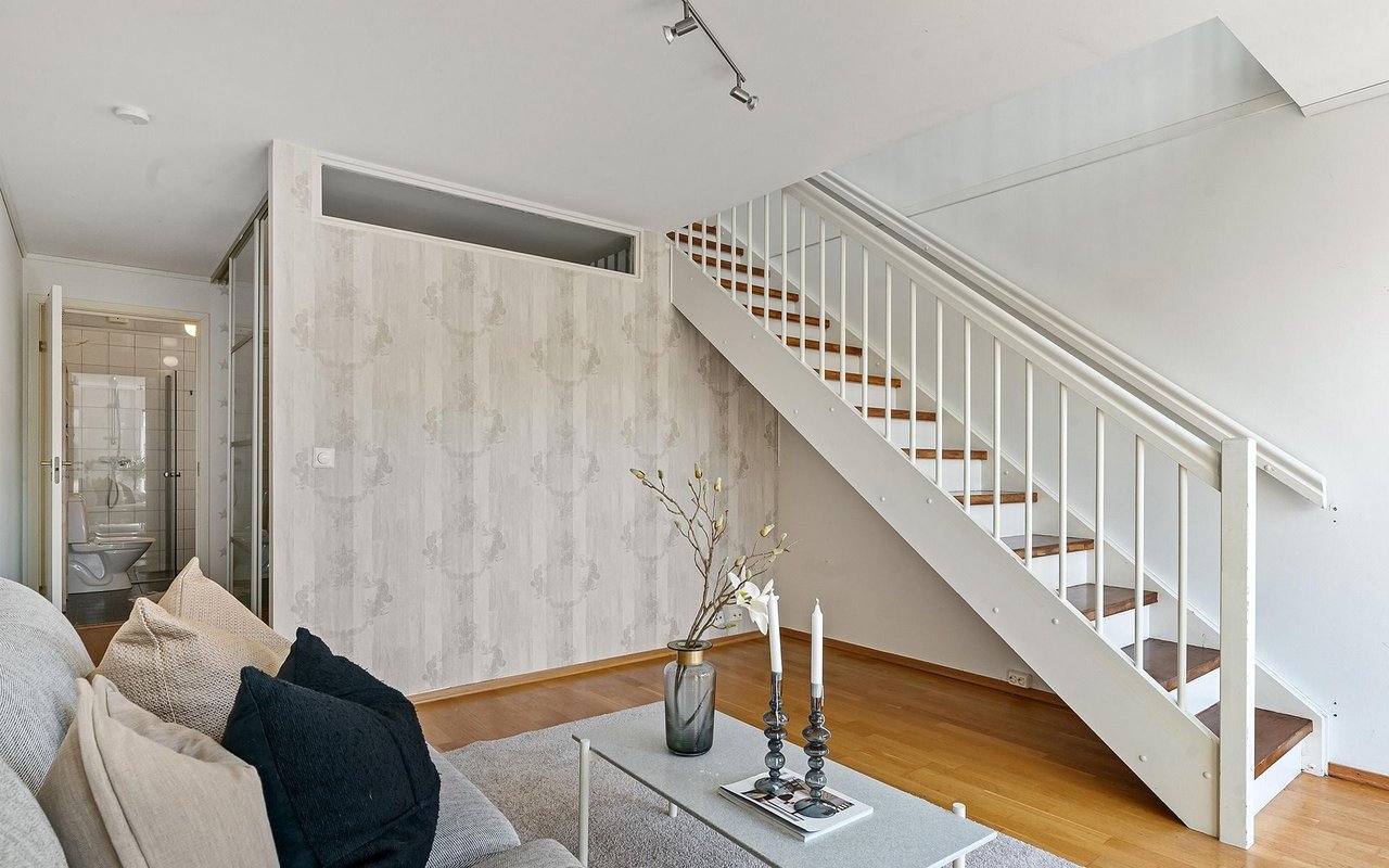Furnished living room with a white staircase, patterned wallpaper, and gray sofa.