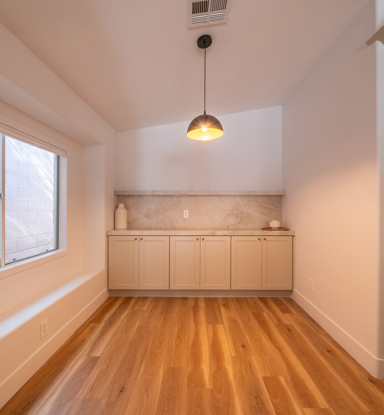 Compact kitchen with pale cabinets, a stone backsplash, pendant light, and wood floors.