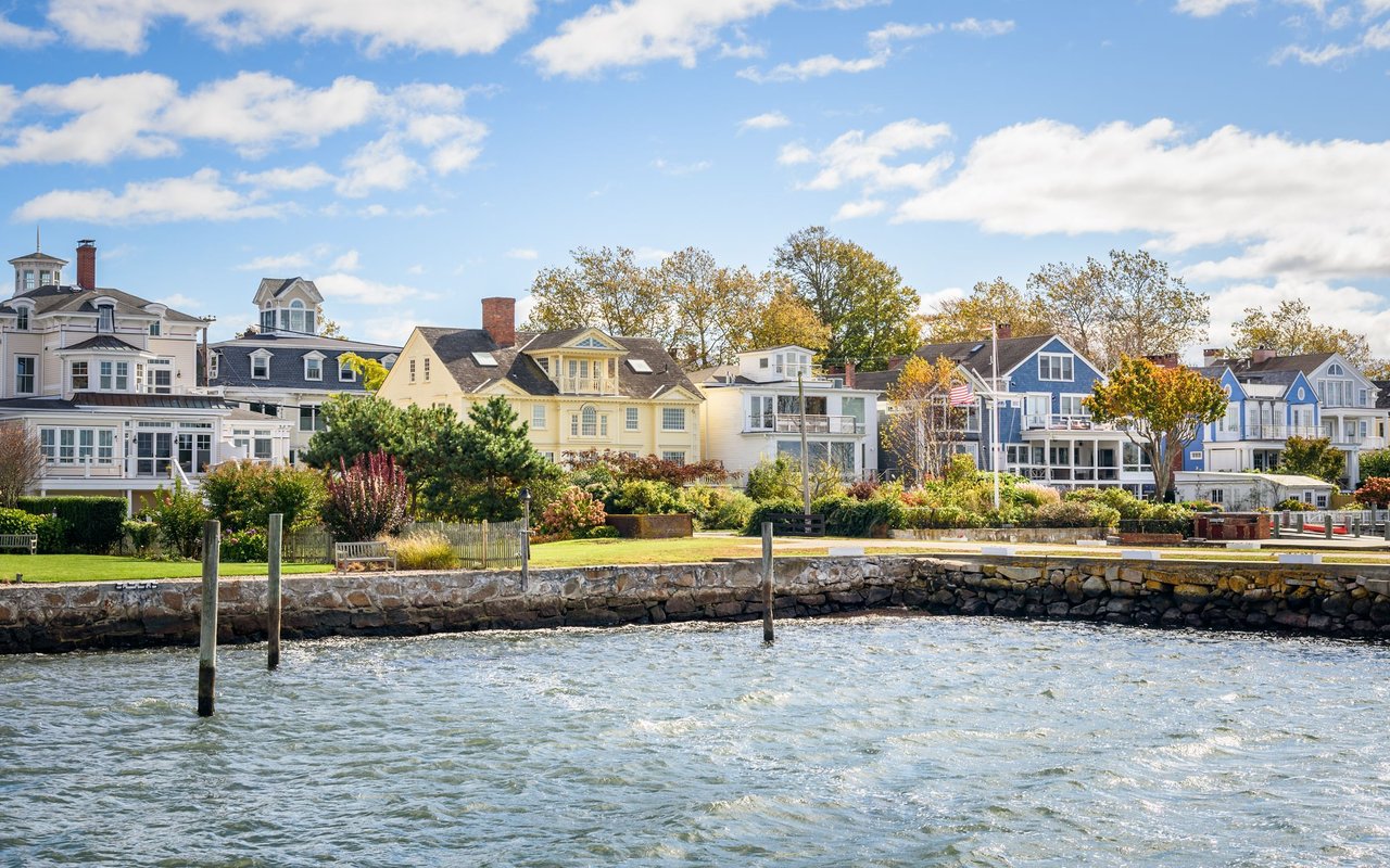 Waterfront neighborhood with colorful homes, a stone seawall, and dock pilings along the shore.