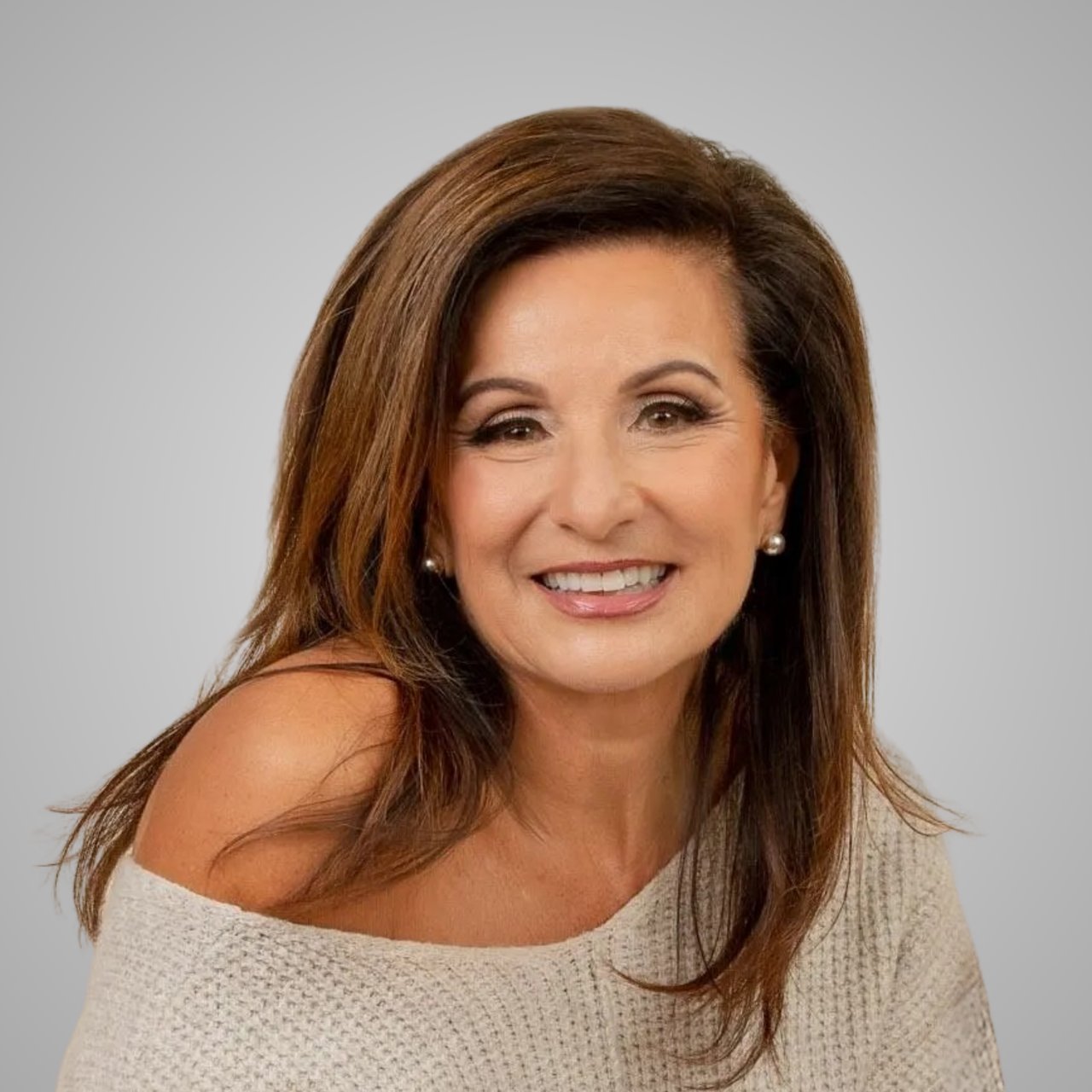 Smiling woman with long brown hair wearing pearl earrings and a cream knit top.