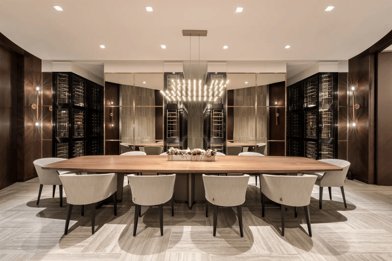 Communal dining room with a long wooden table, chandelier, and wine cabinets.