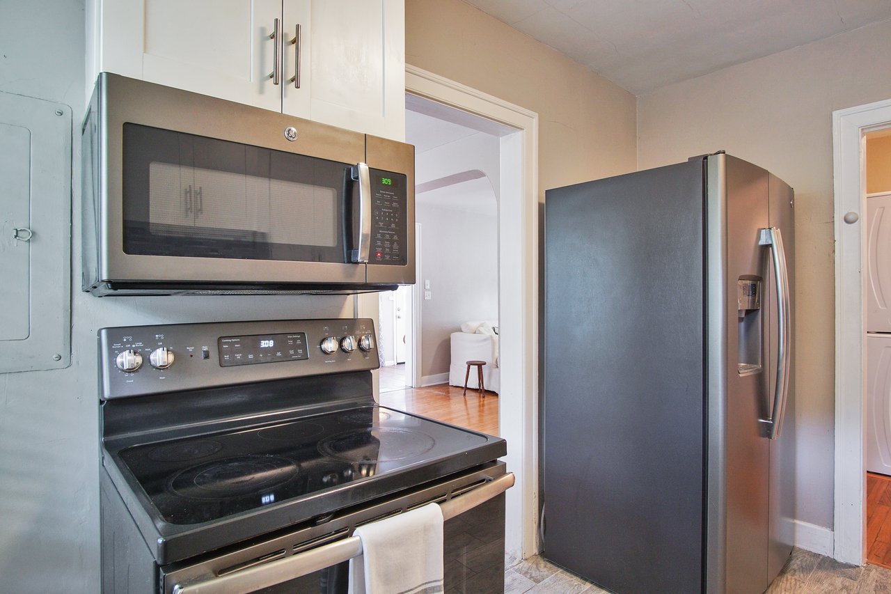 Modern kitchen with stainless steel appliances, including a microwave and oven combo and a refrigerator. A white towel hangs on the oven handle.