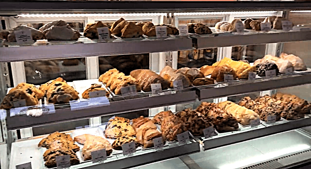 A display case with three shelves of assorted scones arranged in rows.  Each row has a small label in front indicating different flavors.