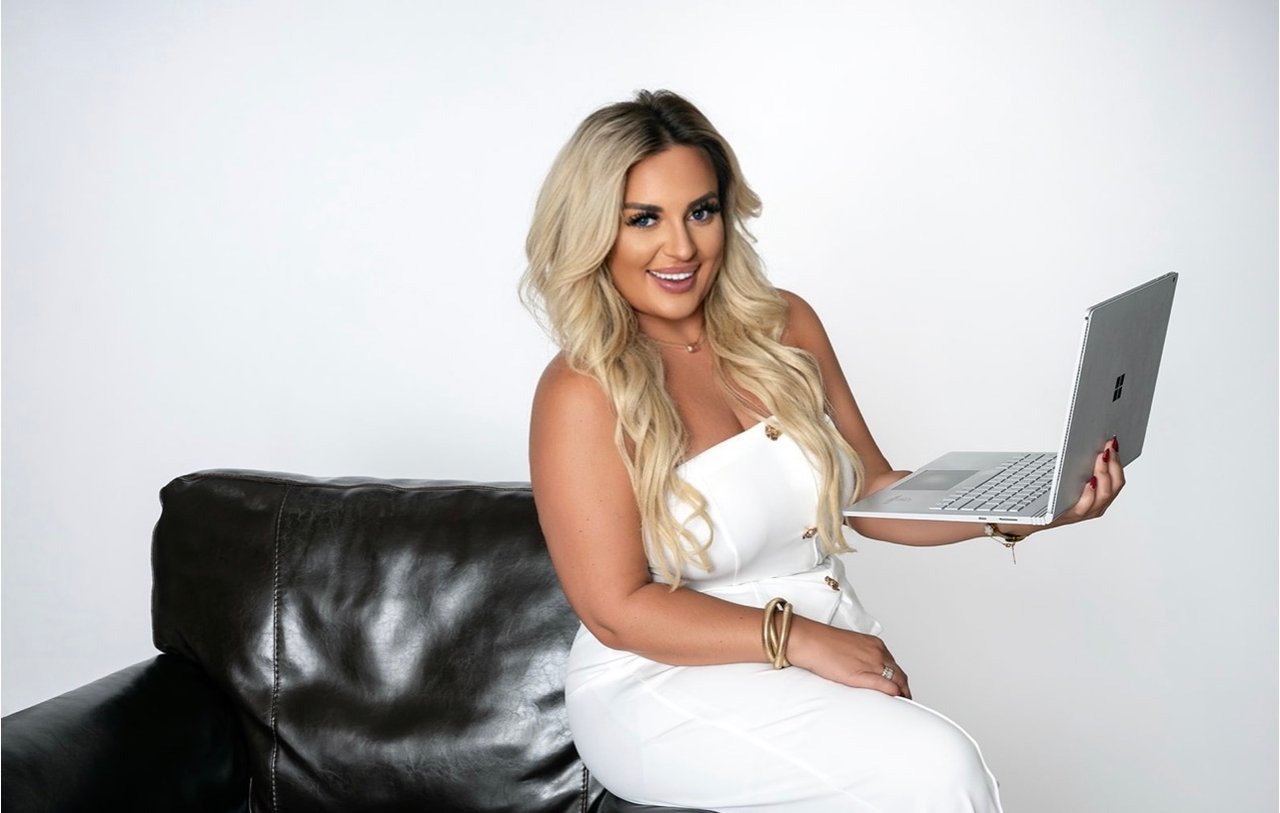 Alexia Goodson seated on a black leather couch, holding an open laptop.