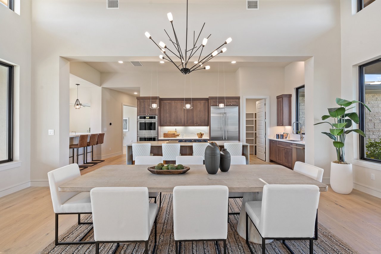 Dining room with a long table and pendant chandelier, open to the kitchen, at this Bee Caves home on Caudill Lane, Austin, Texas.