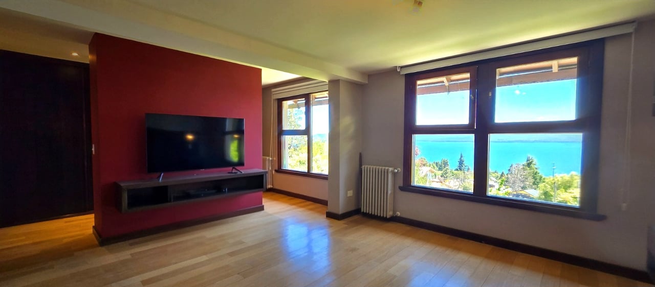 Living room with a red accent wall and large windows overlooking a lake.