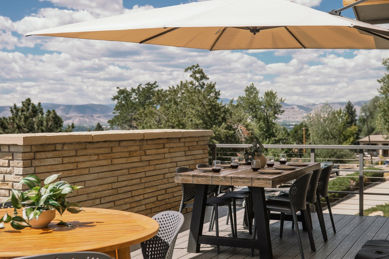 Outdoor dining terrace beneath a large umbrella, with mountain views beyond the railing.