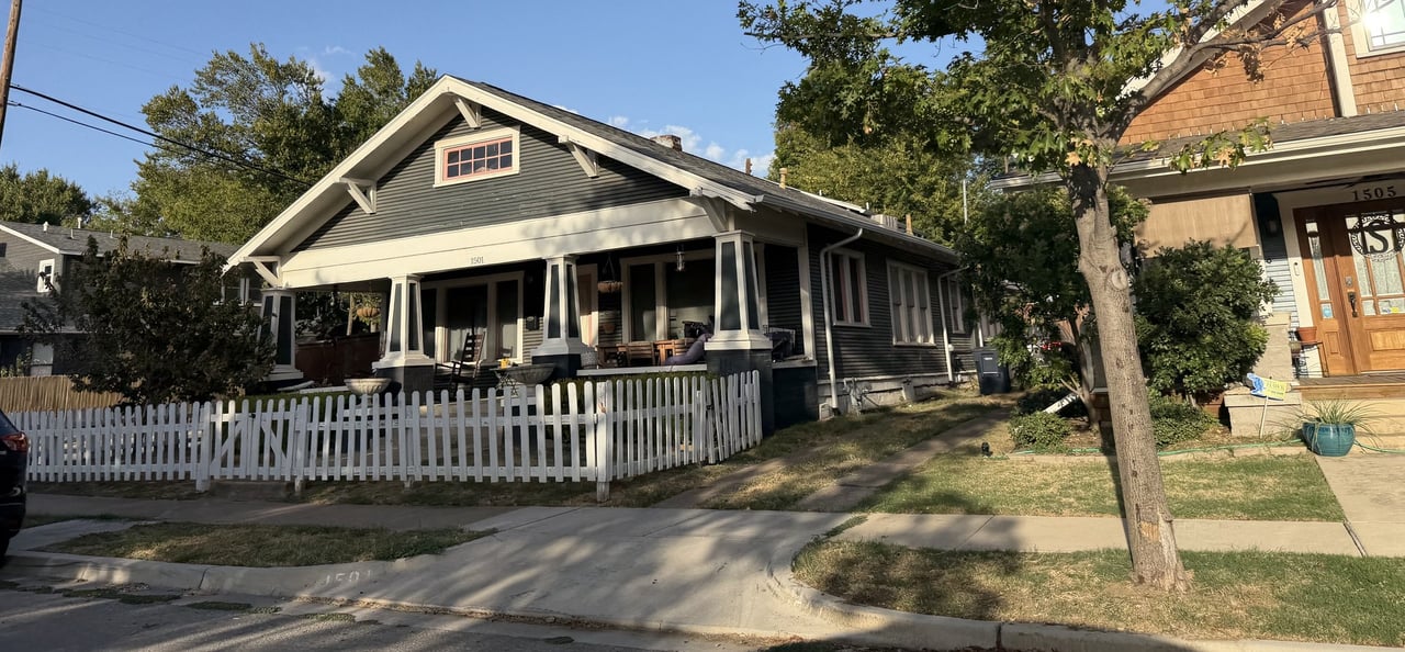 Gray Craftsman bungalow with a broad covered porch and white picket fence.