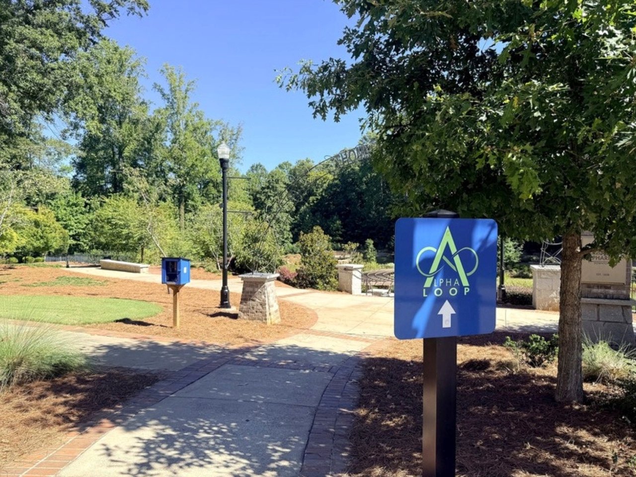 Alpha Loop wayfinding sign beside a shaded pedestrian path.