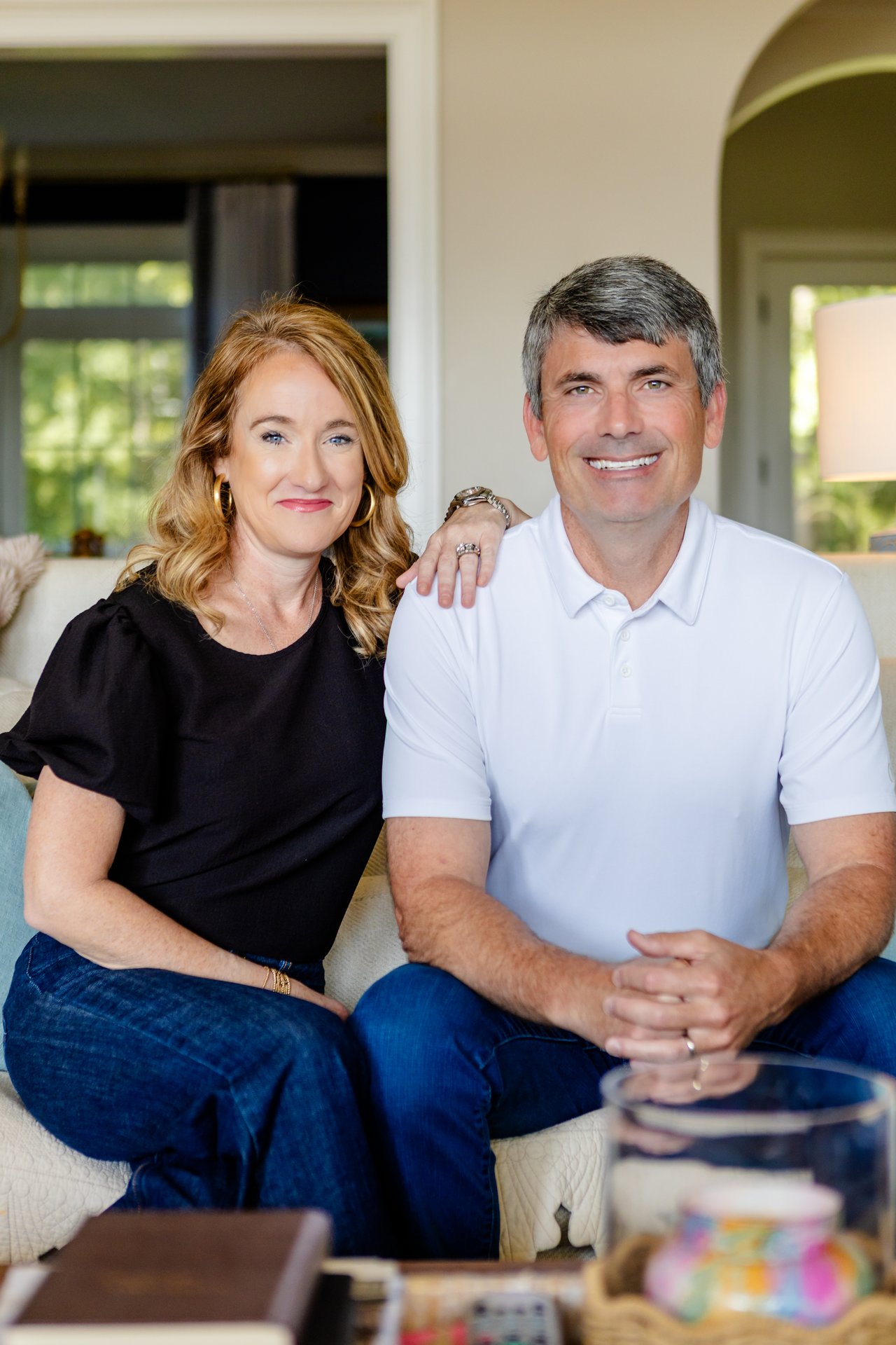 Two smiling real estate agents seated together on a living-room sofa.
