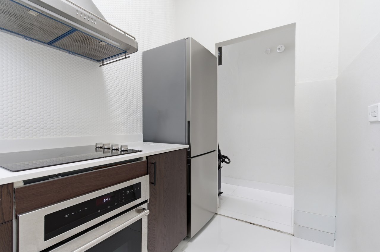 Compact kitchen with stainless steel appliances, dark wood cabinets, and white textured backsplash.