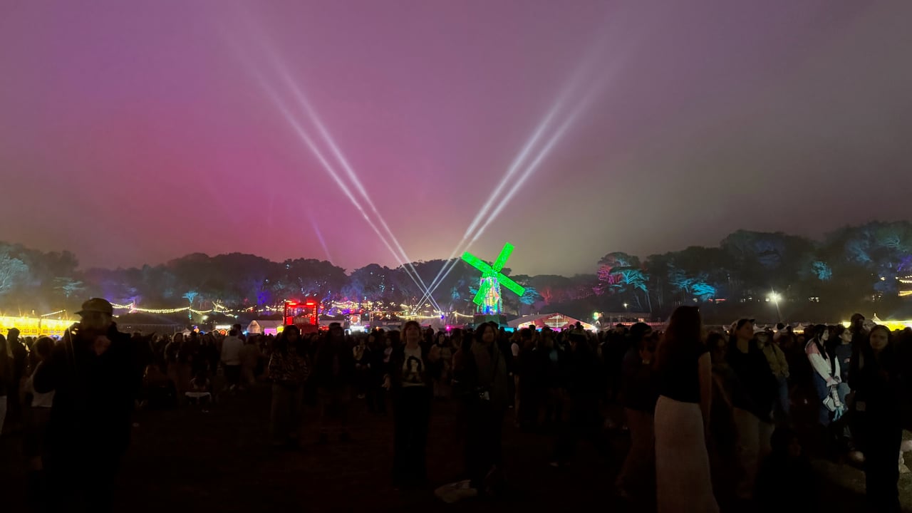 Crowd watching a nighttime festival light show with green laser beams and stage lighting