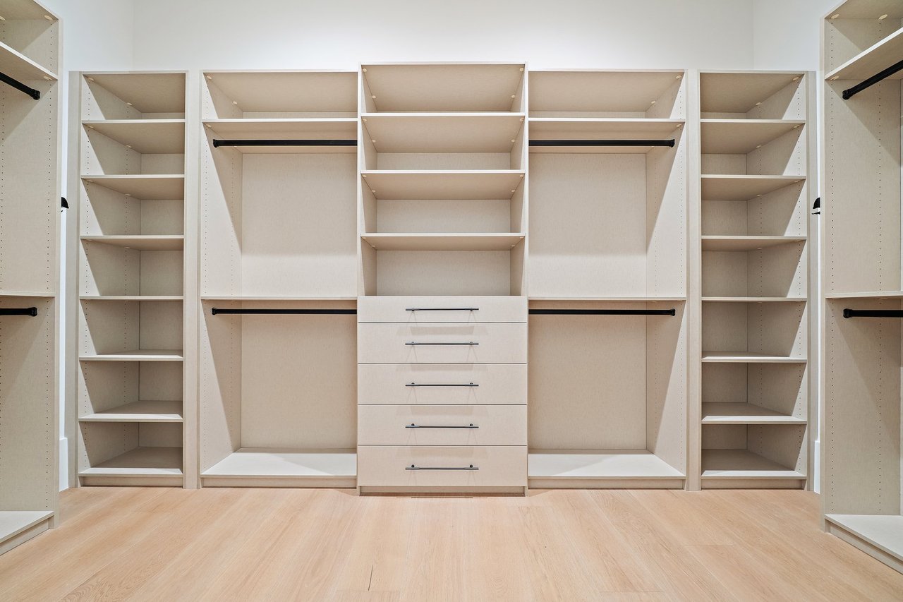 Walk-in closet with built-in shelves, hanging rods, and central drawers.
