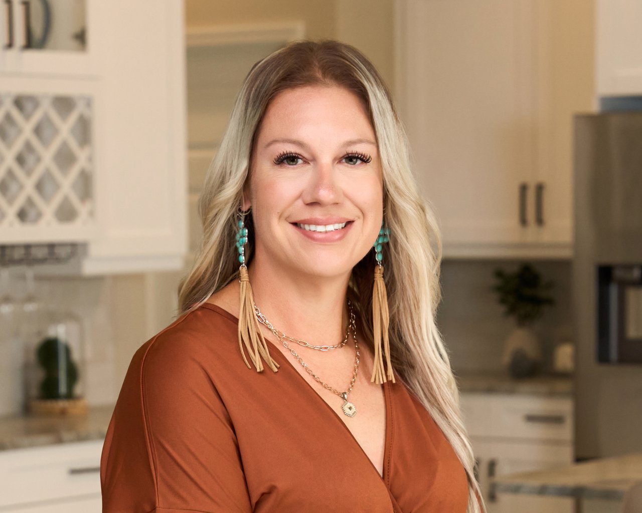 Ashley Casselman smiling in a kitchen, wearing a rust-colored blouse and turquoise earrings.