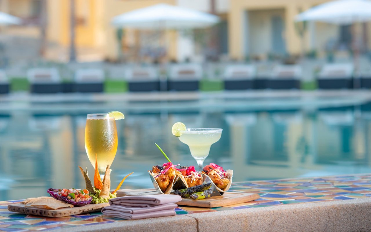 Cocktails and tacos on a tiled pool edge beside a resort swimming pool.