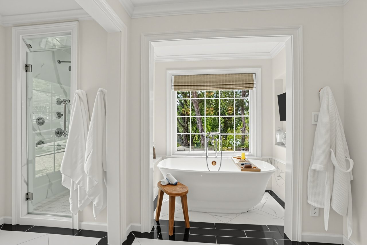 Bathroom with a freestanding soaking tub beneath a window overlooking trees, beside a glass-enclosed shower.