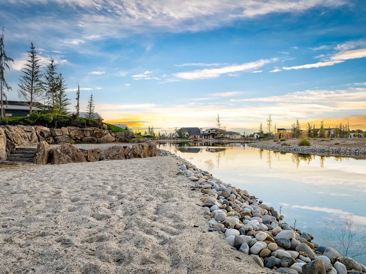 Neighborhood pond with a rocky shoreline and homes reflected in the water at sunset.