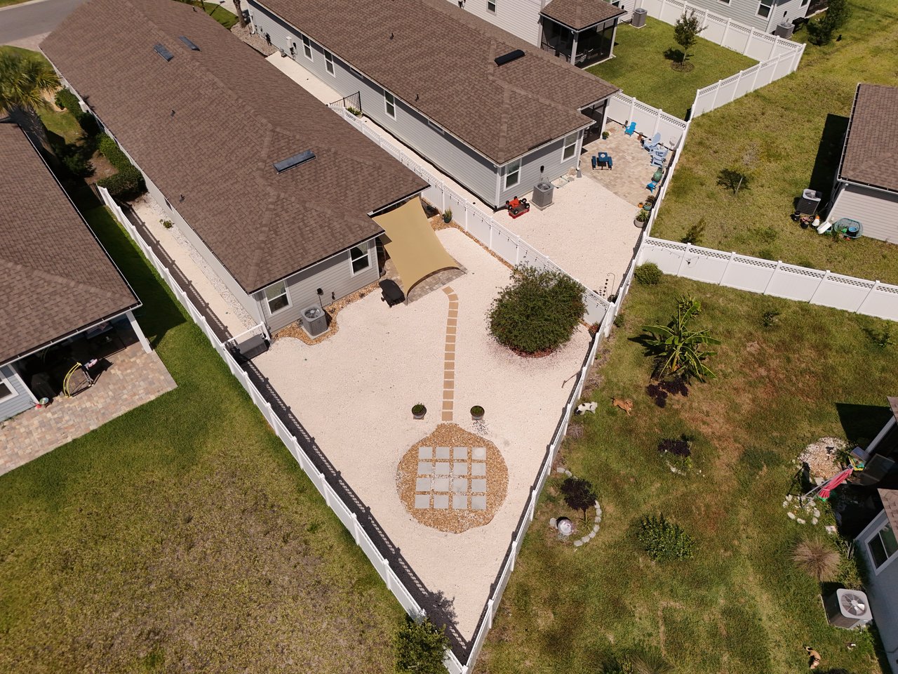 Aerial view of a fenced gravel backyard with a circular paver feature and patio seating.