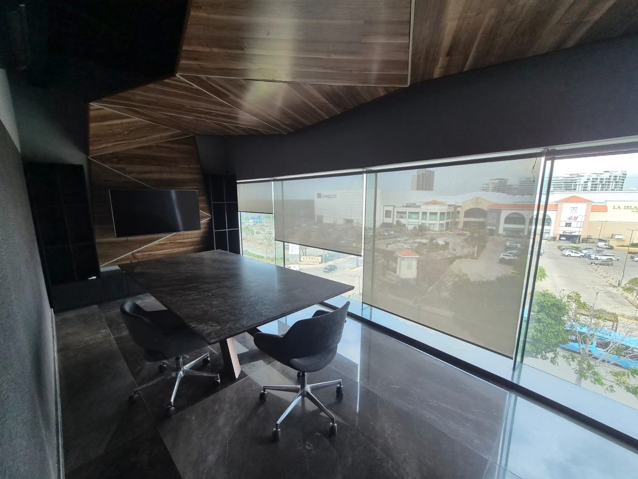 Modern office conference room with a dark stone table, wood paneling, and large windows overlooking commercial buildings.